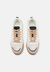 Hvite og beige treningssko med mesh-materiale, svarte detaljer og beige snøringer. Tykk gummisåle med avrundet form.