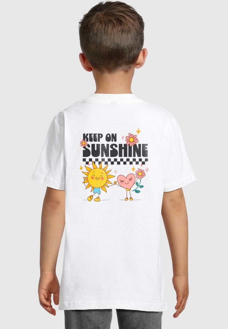 Hvid bomulds t-shirt med et legende print af en sol og et hjerte med blomster, med teksten "KEEP ON SUNSHINE" i fed sorte bogstaver.