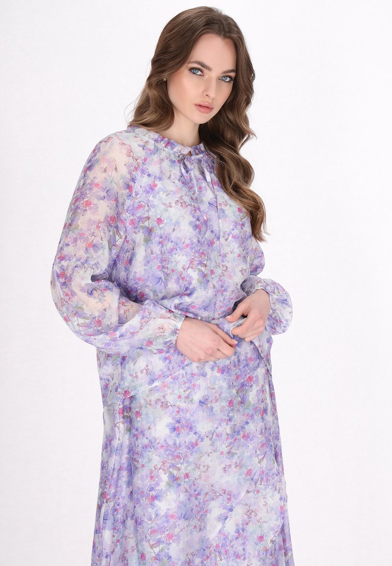 Rochie vaporoasă cu mâneci lungi, în nuanță de mov deschis, cu imprimeu floral. Prezintă un decolteu și un brâu adunat; materialul are o textură ușoară.