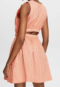 Ensemble deux pièces rayé pêche composé d'un haut court à encolure ronde et d'une jupe évasée. Tissu texturé avec des coutures visibles.