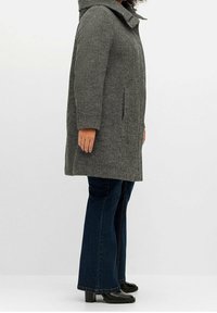 Grijze hooded jas met een textuurpatroon, zijzakken en een rechte snit, gecombineerd met wijde donkere jeans en zwarte enkelboots.