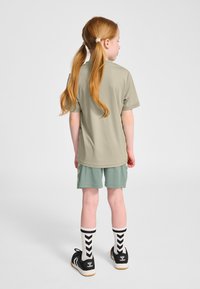 Khakifärgad kortärmad skjorta kombinerad med tealfärgade shorts, med en slät textur. Svarta sneakers med vita och svarta randiga strumpor fulländar looken.