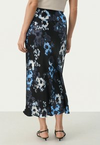 Blommig maxikjol i svart tyg med blå och vita blommönster. Har en åtsittande midja och en svagande nederkant.