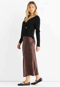 Black knit cardigan with a deep V-neck and gold button detail, paired with a rust satin maxi skirt and black flat shoes. Smooth textures.