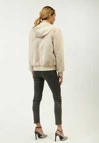 Faux fur cremet jakke med hætte, ribbede manchetter og kant, parret med mørke skinny jeans og sorte hæle med metallisk detalje.