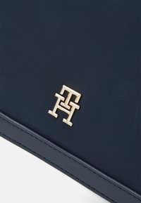 Bolsa de tela azul marino con una superficie texturizada, bordes de cuero liso y un logo en tono dorado destacado en la parte delantera. Diseño simple y moderno.