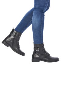 Bottines noires à motif texturé, avec un laçage sur le devant et une fermeture éclair sur le côté. Elles sont dotées d'un talon robuste et d'une boucle en métal en accent.