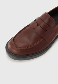 Ruske kožne loafere s okruglim nosom, dekorativnom trakom preko instep-a i fleksibilnom crnom gumenom potplatom. Glatka tekstura s detaljima šavova.