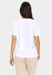T-shirt blanc en coton avec des manches courtes et un col rond. Présente un ourlet droit et un minimum de marque à l'arrière, texture lisse.