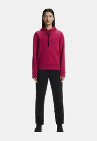 Fuchsiová mikina s kapucňou a klokaním vreckom, čierne šnúrky, v kombinácii s čiernymi nohavicami a čiernymi teniskami. Hladká textúra.