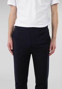 Navy joggebukser laget av myk stoff, med elastisk midje, side lommer, og et tettsittende ben design. Teksturert overflate med sømdetaljer.