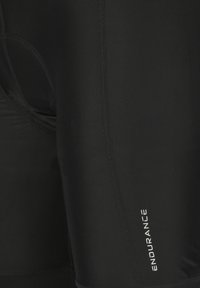 Nærbillede af sorte tætsiddende atletikleggings med flade sømme og hvidt "ENDURANCE"-logo på låret.