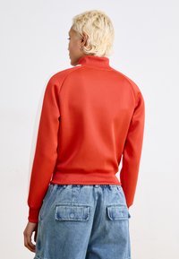 Sweatshirt rouge à col montant avec une finition texturée et des panneaux latéraux blancs. Associé à un short en denim bleu ample avec des poches arrière.