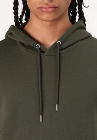 Olive green hoodie made of soft fabric with a v-neckline, featuring silver eyelets and drawstrings for adjustment.