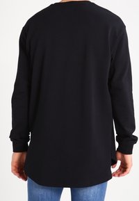 Sudadera negra de manga larga con dobladillo redondeado, fabricada en material suave y con aberturas laterales. Presenta un diseño sencillo y un ajuste holgado.