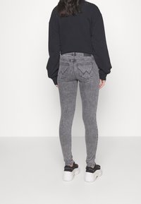 Jeans de tiro alto grises con un ajuste ceñido, que presentan bolsillos traseros con costura en zigzag. La modelo lleva un sudadera negra de corte oversize y zapatillas deportivas.