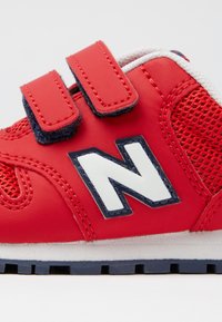Baskets rouges avec une tige en mesh et des superpositions synthétiques. Dotées de deux bandes Velcro, d'un logo blanc et d'une semelle bleu marine.