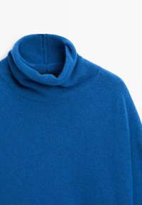 Maglione dolcevita blu lavorato a maglia, disteso su una superficie piana, con collo alto piegato e texture liscia su sfondo bianco uniforme.