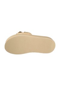 Suola beige di una scarpa con una superficie testurizzata e rigata, caratterizzata da una leggera curvatura. Presenta anche un accento dorato vicino alla parte posteriore.