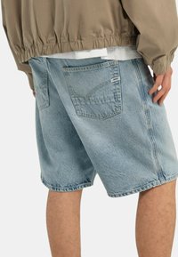 Pantaloni corti in denim blu chiaro con una vestibilità rilassata, orlo sfrangiato e tasche posteriori. Il tessuto presenta un aspetto sbiadito e testurizzato.