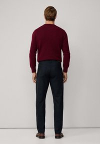 Pull bourgogne et pantalon bleu marine. Le pull a un col rond et des manches longues. Le pantalon a une coupe ajustée et une texture subtile. Chaussures marron.