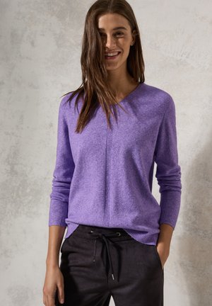 Pull en maille violet avec décolleté en V, poignets côtelés et un détail de couture au centre, associé à un pantalon noir à cordon de serrage. Texture de tissu douce visible.