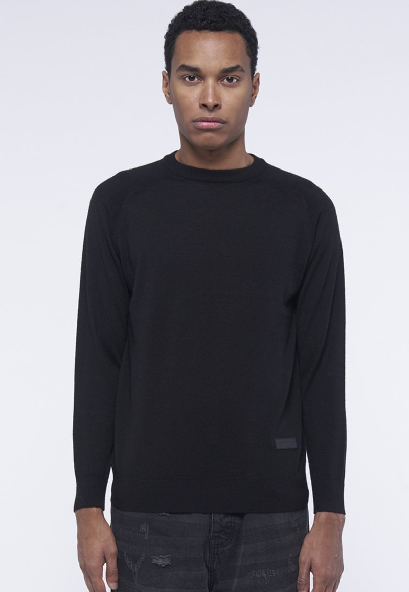 Maglione nero a maniche lunghe con colletto a girocollo, tessuto testurizzato e orlo a coste. Presenta una toppa con logo sul lato sinistro.