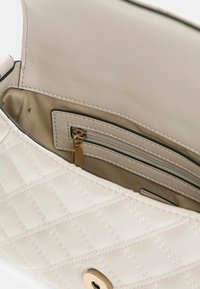 Sac à main crème matelassé avec une fermeture à pression dorée, doté d'un intérieur lisse, d'une poche zippée et de détails de couture à l'extérieur.