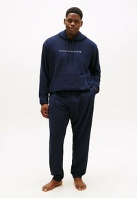 Granatowy hoodie i dopasowane dresy wykonane z miękkiego materiału. Hoodie ma kieszeń na przodzie i logo; spodnie mają elastyczne ściągacze i sznurek w pasie.