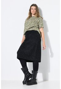 Grünes gemustertes Kurzarmoberteil mit einem schwarzen, knielangen Glitzerminirock und schwarzen High-Heels-Stiefeln. Glatte Textur, lässige Passform.