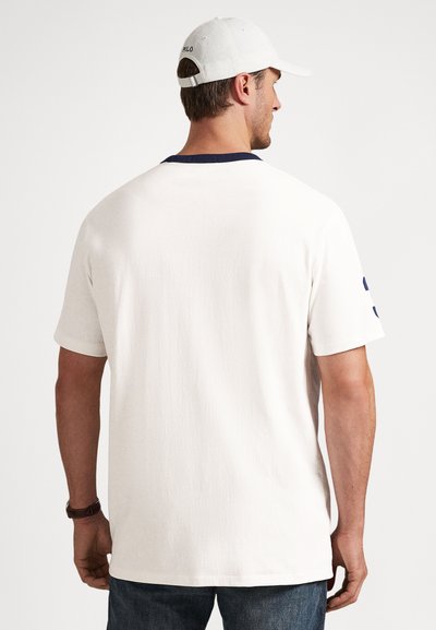 Λευκό βαμβακερό κοντομάνικο μπλουζάκι με ναυτικό μπλε γιακά και κοντά μανίκια. Η πίσω όψη παρουσιάζει μίνιμαλ σχ�εδιασμό και υφασμάτινη υφή. Φοριέται με μπλε τζιν.