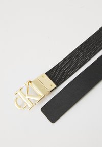 Sort belte med et teksturert mønster, med en gullmetallspenne formet som "CK" og en glatt lærfinish på baksiden.