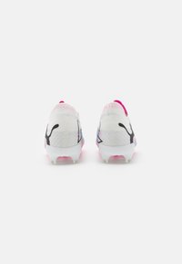 Scarpette da calcio con una parte superiore in mesh bianco, dettagli in logo neri e un tacco rosa; presentano tacchetti in plastica trasparente per una maggiore aderenza.