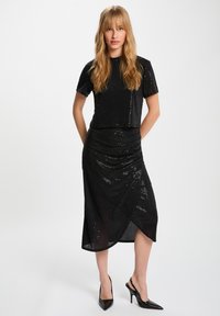 Completo a due pezzi nero con paillettes, composto da un top a maniche corte e una gonna al ginocchio con un design drappeggiato. Texture liscia e silhouette aderente.
