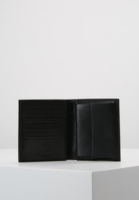 Portafoglio in pelle nera con finitura testurizzata, slot per carte interne e un ampio scomparto. Piegato aperto, che mostra le sue caratteristiche organizzative.