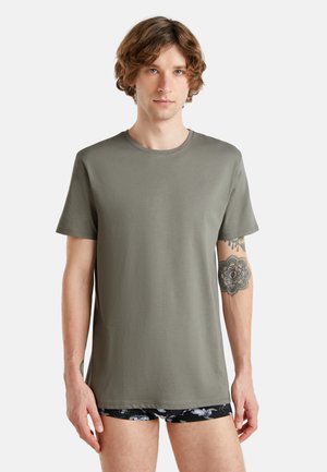 Camiseta de manga corta en verde oliva de tela suave, con cuello redondo y un ajuste relajado. Incluye un patrón floral en los pantalones cortos negros que lleva debajo.