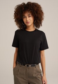 Černé bavlněné tričko s krátkými rukávy, kulatým výstřihem a uvolněným střihem, spárované s khaki kalhotami a černým opaskem s zlatou oválnou sponou.