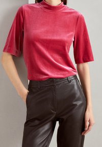 Haut à manches courtes et col montant en tissu doux, ressemblant à du velours, de couleur rose profond. Associé à un pantalon en cuir noir taille haute.