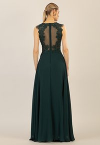 Langes smaragdgrünes Abendkleid mit tailliertem Oberteil, transparenter Rückseite und floralen Spitzelementen. Fließender Rock mit einem verdeckten Reißverschluss im Rücken.