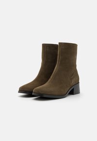 Botas de tobillo de ante marrón con punta cuadrada y tacón bloque, que presentan un acabado liso y texturizado y un diseño minimalista.