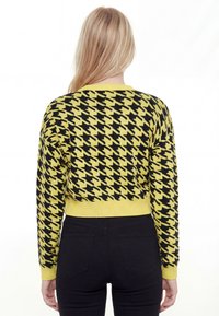 Žltý a čierny krátky sveter s kockovaným vzorom houndstooth, dlhými rukávmi a rebrovanými manžetami. Mäkká pletená látka, okrúhly výstrih a priliehavý strih.