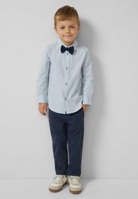 Lichtblauw overhemd met knopen, marineblauwe broek, marineblauwe vlinderdas en witte sneakers met een gestructureerde zool. Glad materiaal en een vakkundige pasvorm.