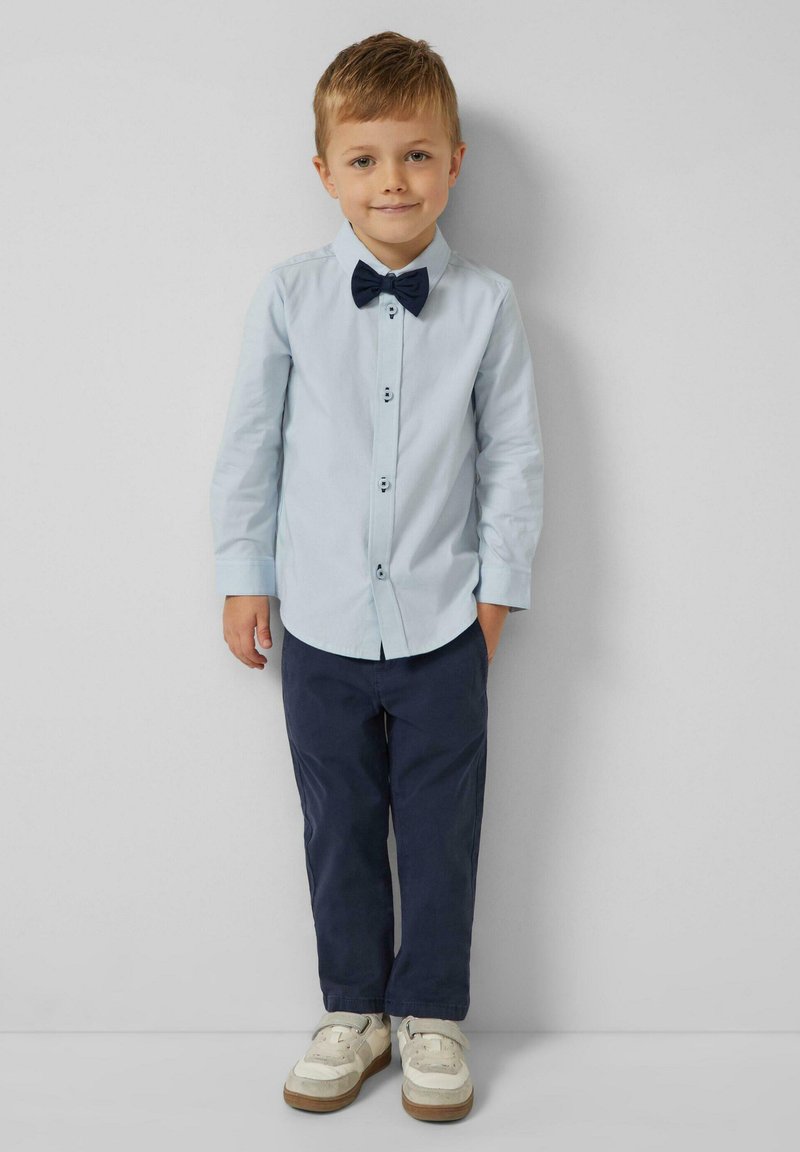 Lichtblauw overhemd met knopen, marineblauwe broek, marineblauwe vlinderdas en witte sneakers met een gestructureerde zool. Glad materiaal en een vakkundige pasvorm.