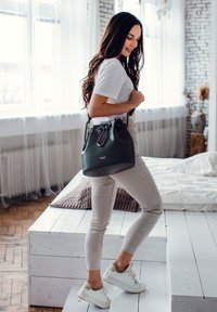 Černá kožená kabela ve tvaru kbelíku s uzávěrem na šňůrku, stříbrnými doplňky a logem. Model nosí bílé tričko, světlé úzké kalhoty a bílé tenisky.