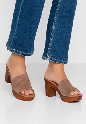 Escarpins à bout ouvert avec une tige en daim couleur tan et un talon bloc en bois. Les chaussures présentent des brides larges et un design à bout arrondi et lisse.