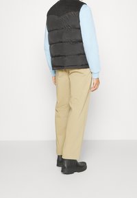 Gilet imbottito nero con yoke in velluto a coste, indossato sopra un maglione azzurro chiaro, abbinato a pantaloni beige e stivali neri alla caviglia.