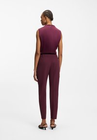 Burgundy sleeveless top with subtle back zipper, paired with fitted burgundy trousers. Smooth fabric and tailored silhouette. Black sandals.