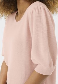 Jasnoróżowy dzianinowy top z okrągłym dekoltem, krótkimi bufkami i luźnym krojem. Teksturowana tkanina, subtelne prążkowane detale.