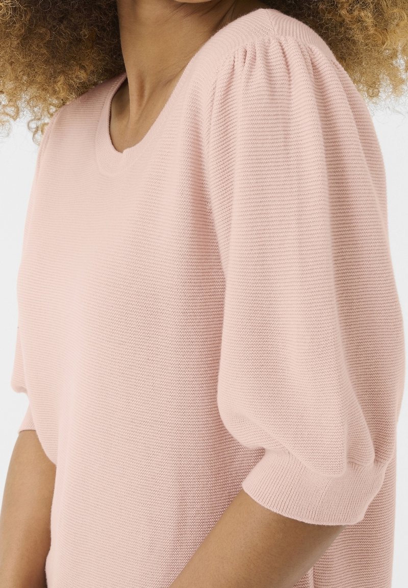 Jasnoróżowy dzianinowy top z okrągłym dekoltem, krótkimi bufkami i luźnym krojem. Teksturowana tkanina, subtelne prążkowane detale.