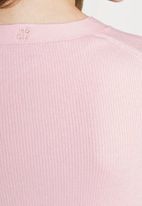 Tejido de suéter de color rosa con textura acanalada, mostrando un escote redondo y un sutil logo en la parte posterior, con una textura fina y bordes limpios.